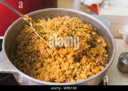 La cuisson pilaf oriental dans la cuisine dans la vasque. Une femme prépare un plat d'agneau, boeuf, riz, pois chiches, les carottes dans une grande casserole. Banque D'Images