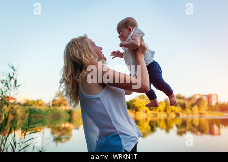 Jeune mère marcher par la rivière d'été avec bébé fille. Woman lifting kid et d'avoir du plaisir à l'enfant. Famille passe du temps ensemble Banque D'Images