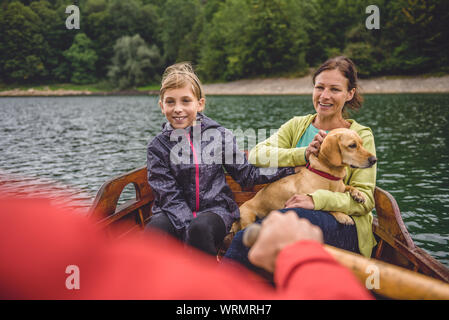 Famille avec le petit chien jaune de l'aviron sur le lac de montagne dans un bateau Banque D'Images