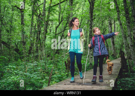Mère et fille avec petit chien jaune de la randonnée sur un sentier en forêt Banque D'Images