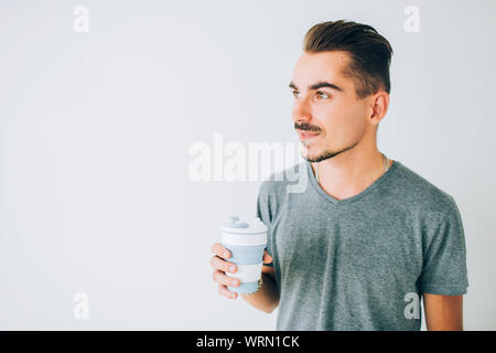 Beau jeune gars en t-shirt gris tenant une tasse de café sur fond blanc isolé. À côté. Banque D'Images