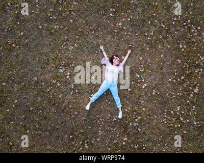 Cute girl allongé dans l'herbe au cours de l'automne aerial Banque D'Images