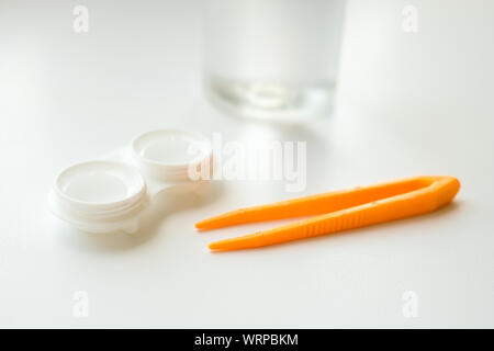 Accessoires pour une utilisation correcte des lentilles de contact : boîtier, brucelles et flacon de solution sur fond blanc. Correction de la vision en toute sécurité. Mise au point sélective. Banque D'Images