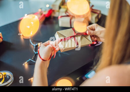 Jeune femme est présente d'emballage. Présent enveloppé dans du papier craft avec un ruban rouge et or pour Noël, anniversaire, fête des mères ou la saint valentin Banque D'Images