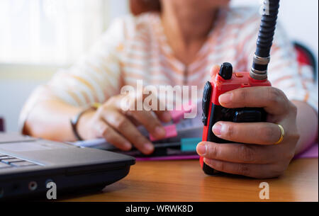 En utilisant l'opérateur radio femelle talkie - walkie pour communiquer avec d'autres personnes et de travailler avec le document sur un bureau de travail, communication concept. Banque D'Images