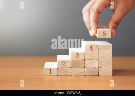 Par contre les femmes de mettre une cale en bois sur le dessus et l'arrangement des blocs en bois en bois d'empilage sur table en forme d'un escalier, un concept d'affaires La croissance de Banque D'Images