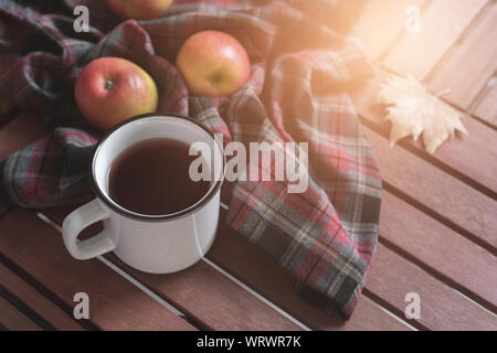 Les mains avec du thé chaud, le bloc-notes de couverture à damier vide pommes et feuilles d'automne sur fond de bois ancien Vintage tonning concept d'automne Banque D'Images