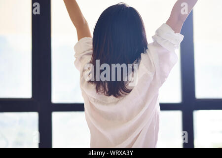 Vue arrière d'une jeune femme asiatique qui s'étend elle-même dans la chambre Banque D'Images