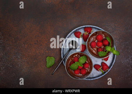 La mousse au chocolat avec des framboises dans des verres en verre servant sur un fond en béton brun. Vue de dessus. copy space Banque D'Images