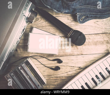 Ensemble d'appareil audio, microphone, écouteurs, cassette, piano et denim sac à l'arrière-plan en bois vintage Banque D'Images