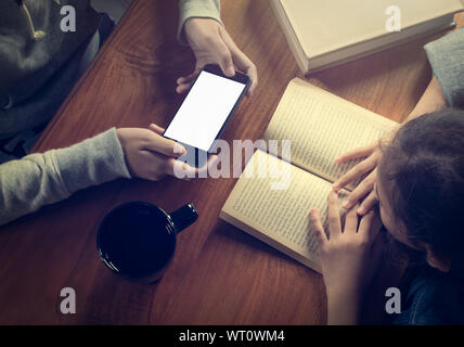 Jeune fille lisant un livre et une autre fille holding smart phone sur table en bois avec Coffee cup Banque D'Images