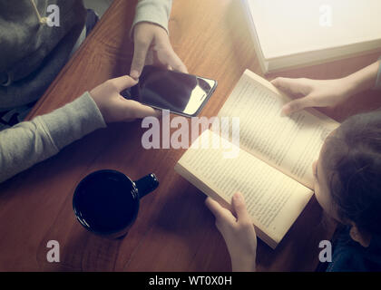 Jeune fille lisant un livre et une autre fille holding smart phone sur table en bois avec Coffee cup Banque D'Images