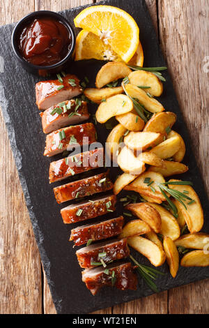 Filet de porc cuit savoureux dans le miel-orange déglacer avec les quartiers de pommes de terre sur une assiette sur la table. Haut Vertical Vue de dessus Banque D'Images