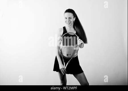 Portrait noir et blanc de belle jeune femme dans des vêtements de sport holding tennis racket debout contre l'arrière-plan blanc. Banque D'Images