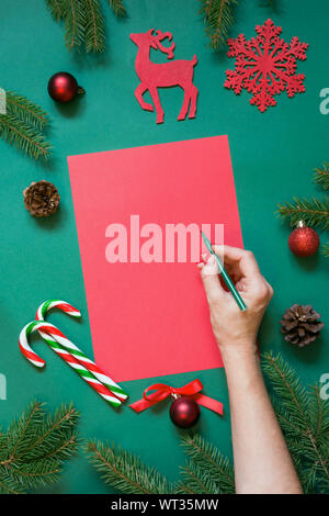 Noël rouge blanc pour lettre au père ou votre liste de cadeaux ou activités de l'avent sur vert. La main féminine par écrit. Vue d'en haut. Mise à plat. Banque D'Images