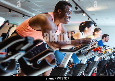 L'homme d'Afrique et d'amis sur le vélo de remise en forme dans la salle de sport Banque D'Images