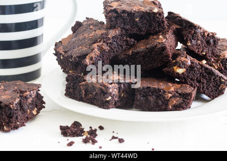 Brownies au chocolat dans une pile sur plaque blanche avec noir et blanc tasse à café de flou artistique en arrière-plan sur fond blanc Banque D'Images