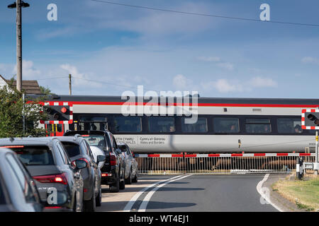 La file de voitures à un passage à niveau qu'un train passe. Pays de Galles, Royaume-Uni. Banque D'Images