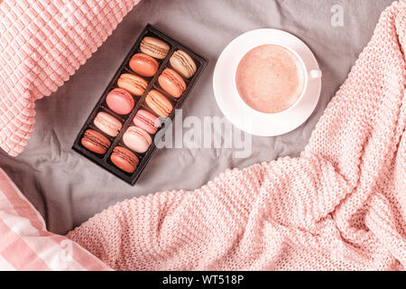 Lit avec plaid en tricot rose, café et macarons, vue du dessus, copiez l'espace, mise à plat. Banque D'Images