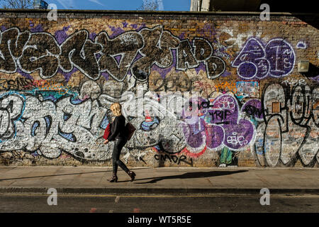 Une jeune femme passe devant un mur de graffiti près de Brick Lane à Londres. Crédit photo : Brian Hickey/Alamy Banque D'Images