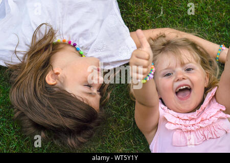 Deux petites filles portant sur l'herbe, riant et montrant Thumbs up Banque D'Images