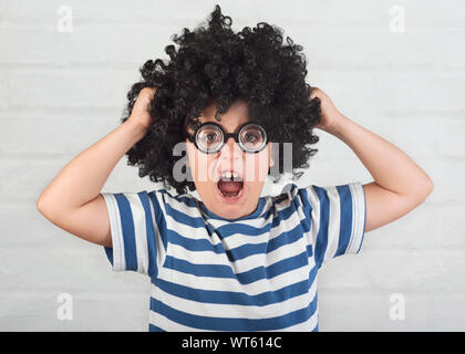 Angry boy wearing lunettes nerd qui tire ses cheveux sur fond brique Banque D'Images