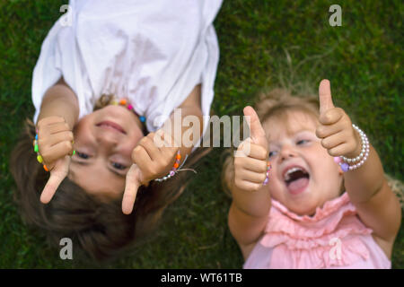 Deux petites filles portant sur l'herbe, riant et montrant Thumbs up Banque D'Images