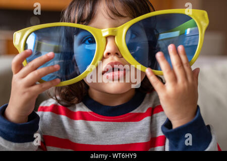 Adorable petite fille jouant avec des lunettes de la nouveauté à la maison Banque D'Images