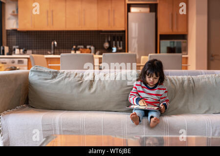 Jolie petite fille assise sur son canapé à l'aide d'une tablette Banque D'Images