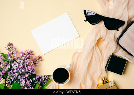 24 féminin avec carte blanche, papier de soie, flacon de parfum, tasse de café, des lunettes de soleil et de lilas fleurs sur fond beige. Vue de dessus, les minimums d'offres Banque D'Images