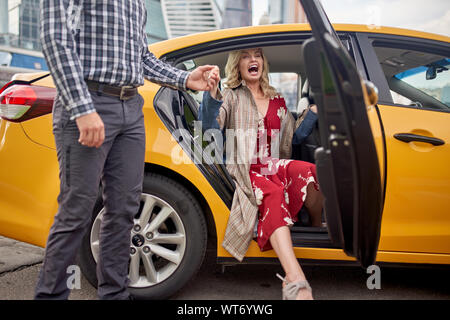 Photo d'un homme donnant la main pour femme blonde en robe longue in taxi en après-midi Banque D'Images