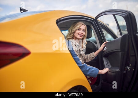 Photo de blonde sitting in back seat of taxi jaune avec porte ouverte pendant la journée. Banque D'Images