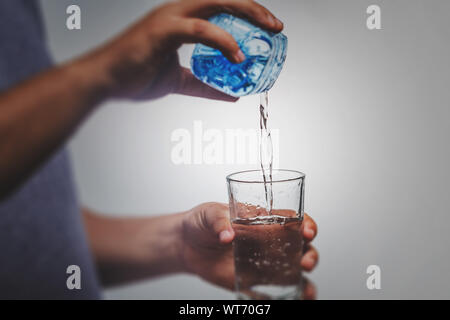 Woman's hand holding une bouteille d'eau verser de l'eau dans un verre sur fond blanc - style de vie sain Banque D'Images