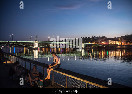 LYON, FRANCE - 18 juillet 2019 : les Français, surtout les hommes assis sur la rive du Rhône (quais) dans la soirée, boire de l'alcool tandis que les gens sont Banque D'Images