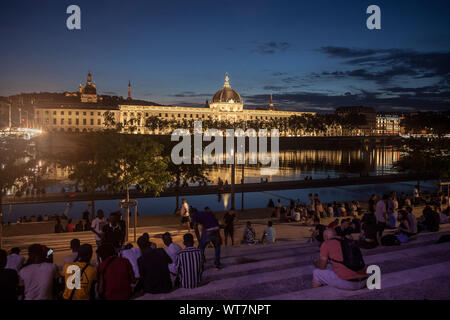 LYON, FRANCE - Juillet 18, 2019 : Le français des gens assis sur la rive de la quais de Rhône, en face de l'Hôtel-Dieu, l'un des principaux monuments de la ville f Banque D'Images