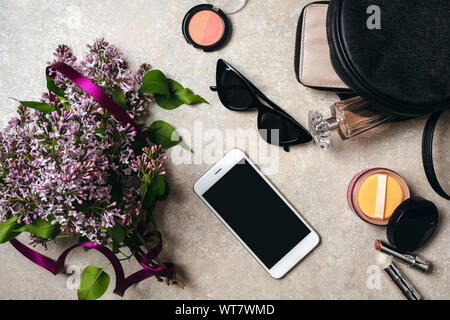 Mise à plat de l'espace de bureau moderne accueil minimal avec des fleurs lilas, lunettes, smartphone, sac en cuir, porte-monnaie, cosmétiques, parfum femme sur le béton backg Banque D'Images