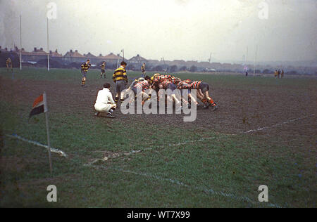 Années 1960, historiques, match de rugby amateur à Wallasey, Wirral, England UK, à l'extérieur sur un terrain boueux, les joueurs masculins s'accroupit dans une mêlée vu par l'arbitre. Banque D'Images