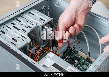 Main de l'homme branché à l'interface SATA (Serial ATA), l'accessoire câble de données série dans disque dur. Interface de bus d'ordinateur pour connecter les périphériques de stockage de masse, Banque D'Images