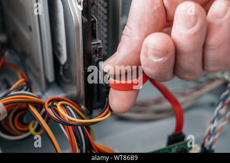 Main de l'homme branché à l'interface SATA (Serial ATA), l'accessoire câble de données série dans disque dur. Interface de bus d'ordinateur pour connecter les périphériques de stockage de masse, Banque D'Images