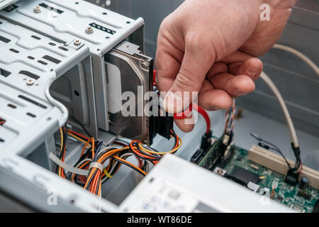 Main de l'homme branché à l'interface SATA (Serial ATA), l'accessoire câble de données série dans disque dur. Interface de bus d'ordinateur pour connecter les périphériques de stockage de masse, Banque D'Images