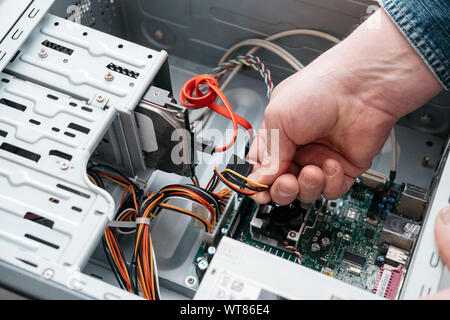 Main de l'homme branché à l'interface SATA (Serial ATA), l'accessoire câble de données série dans disque dur. Interface de bus d'ordinateur pour connecter les périphériques de stockage de masse, Banque D'Images