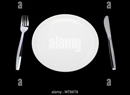 Couvert, assiette blanche, couteau et fourchette sur un fond noir Banque D'Images