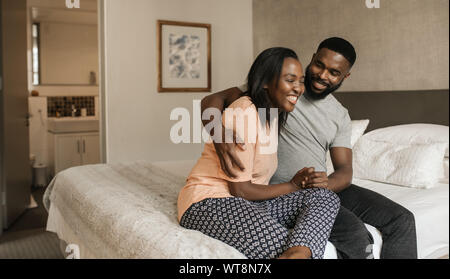 Young African American couple assis sur leur lit et rire ensemble Banque D'Images