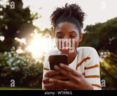 Portrait d'une jeune femme afro-américaine à l'aide de téléphone mobile dans le parc aux beaux jours smiling - très heureux woman on cellphone Banque D'Images