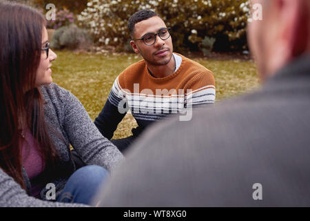 Beau jeune homme africain siégeant ensemble avec des amis multiracial dans le parc Banque D'Images