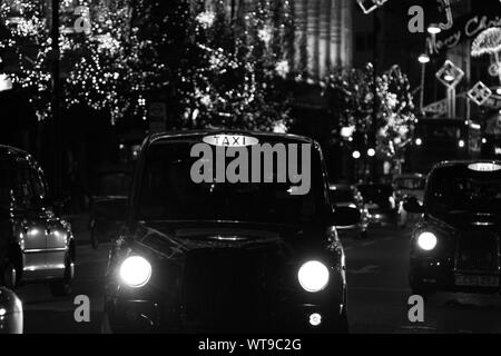 IMAGE NOIR ET BLANC AUTHENTIQUE DE LONDON TAXIS TRAVAILLANT DANS OXFORD STREET, LONDRES LA NUIT AU COURS DE LA PÉRIODE DE VACANCES DE NOËL. Décoration de Noël lumières de rue LE LONG DE LA RUE. Les images monochromes. La vie de la rue. La vie en ville. Scène urbaine de nuit. CHRITMAS. Banque D'Images