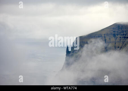 Paysages de l'antenne de nuages couvrant énorme falaise rocheuse au-dessus de l'eau sur la mer des îles Féroé Banque D'Images