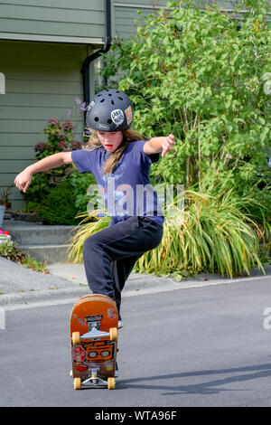 Jeune garçon aux cheveux long sur la planche à roulettes rue résidentielle. Banque D'Images