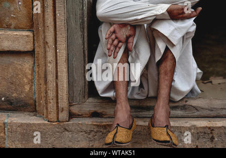 L'homme assis à la porte de sa maison portant des chaussures majori Banque D'Images