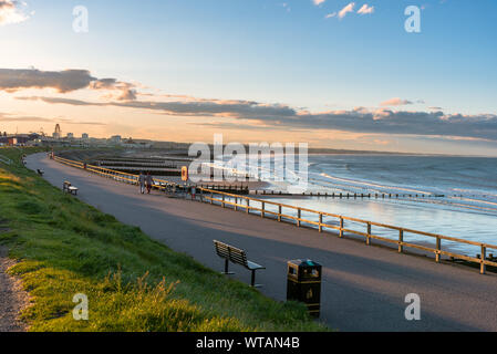 Clôturé allée bordée de bancs sur une digue le long d'une plage de sable fin au coucher du soleil Banque D'Images